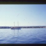 Segelboot im Hafen mit Küstenlinie und Häusern am Mittelmeer