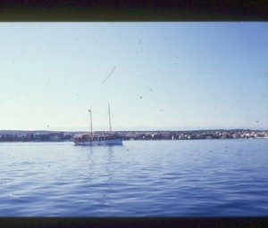Segelboot im Hafen mit Küstenlinie und Häusern am Mittelmeer