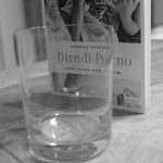 Buch "Dirndl Porno" von Andreas Karosser auf Tisch neben Wasserglas, Schwarzweiß-Fotografie