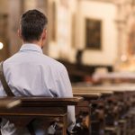 Mann sitzt nachdenklich in einer Kirchenbank und schaut nach vorne, religiöse Kontemplation in sakralem Raum