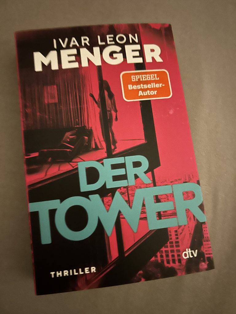 Buchcover von ‚Der Tower‘, einem Thriller von Ivar Leon Menger, mit markantem Design: Der Titel ‚Der Tower‘ ist in großen, türkisfarbenen Lettern auf rot-schwarzem Hintergrund gedruckt, während der Autorname ‚Ivar Leon Menger‘ in Weiß daneben steht. Im Hintergrund erkennt man eine stilisierte, düstere Hochhaussilhouette. Das Cover trägt zudem ein orangefarbenes Siegel mit der Aufschrift ‚Spiegel-Bestseller-Autor‘.