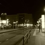 Nächtliche Straßenbahnhaltestelle in Frankfurt mit beleuchteten Hochhäusern, Passanten und moderner Stadtarchitektur