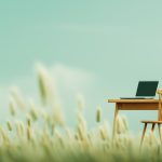 Minimalistischer Arbeitsplatz mit Laptop auf Holztisch inmitten von Grasfeld unter türkisem Himmel