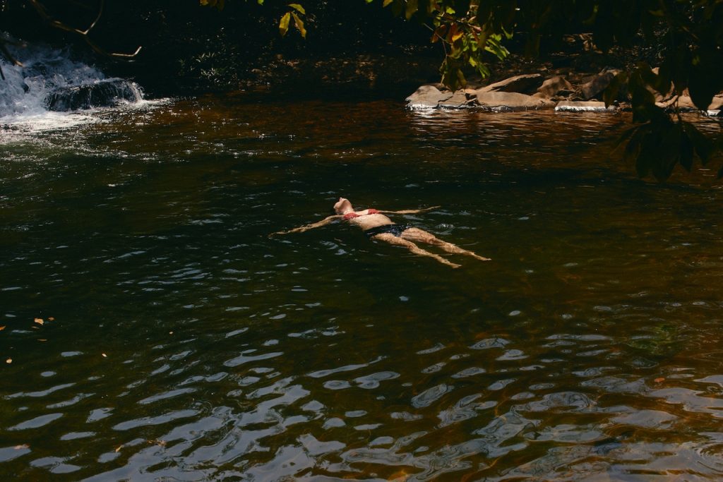 Mann schwebt entspannt im klaren Fluss, umgeben von Felsen und grüner Natur, Naturgewässer Badevergnügen