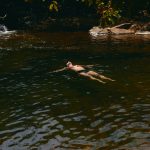 Mann schwebt entspannt im klaren Fluss, umgeben von Felsen und grüner Natur, Naturgewässer Badevergnügen